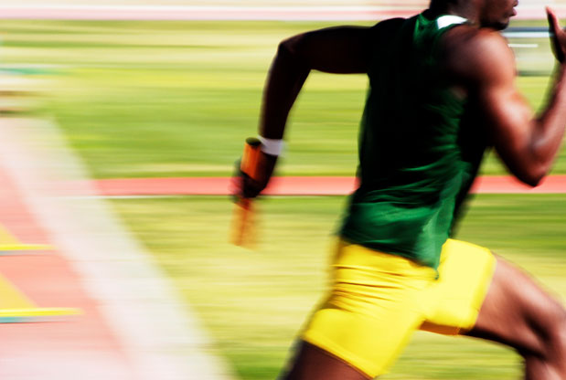 A sprinter in a green top and yellow shorts runs on a track, holding a baton during a relay race. Think of it as mastering the art of movement, much like using three Photoshop tricks to enhance and extend your images with precision and efficiency.