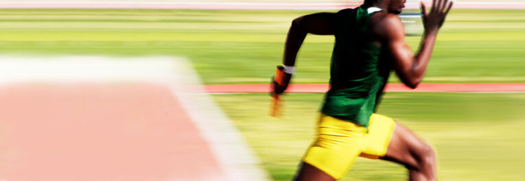 A sprinter wearing a green top and yellow shorts runs on a track while holding a baton during a relay race, showcasing movements so dynamic they could inspire Three Photoshop Tricks to Enhance and Extend Your Images.