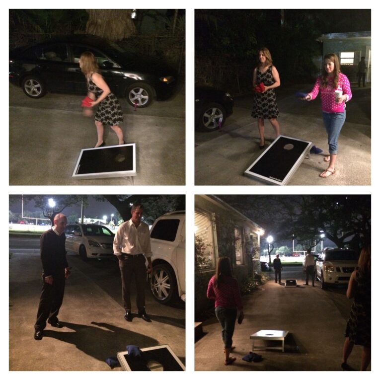 Four people are playing cornhole in a dimly lit driveway at night, sporting a mix of casual and dressed-up attire. It's the PaperStreet Holiday Party 2014 - Ugly Sweaters Gifts & Meat, with a black car and two white cars parked nearby.