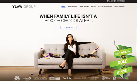 A woman in formal attire sits on a grey couch with chocolate boxes around her. YLaw Group branding and contact number are visible. A "2015 MarCom Gold Winner" ribbon is displayed in the corner.