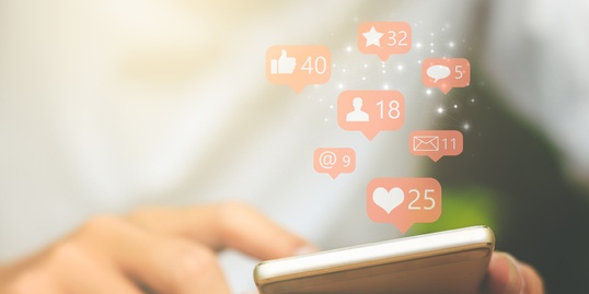 Close-up of a person using a smartphone with various social media notifications, including likes, comments, messages, and followers, appearing above the screen.