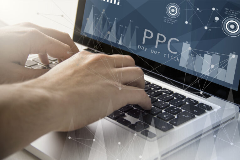 Hands typing on a keyboard with a computer screen displaying "PPC pay per click" and various charts and graphs in the background.