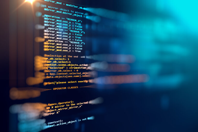 A close-up view of a computer screen displaying lines of code in various colors, indicating programming or software development work. The background is blurred.