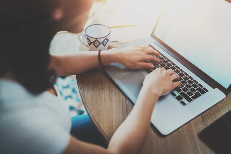 Person typing on a laptop at a wooden table with a coffee cup nearby.
