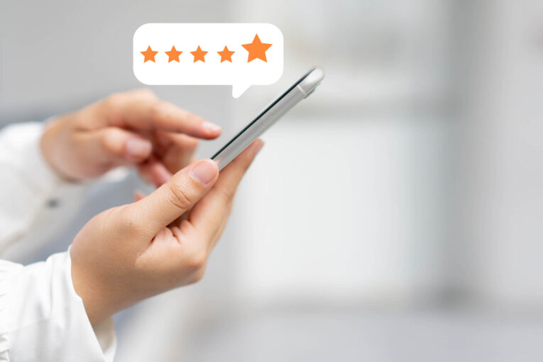 A person holding a smartphone with a 5-star rating icon displayed above it, indicating positive feedback or review.