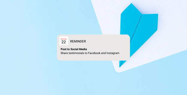 A reminder notification on a blue and white background reads: "Post to Social Media. Share testimonials to Facebook and Instagram." A blue paper airplane lies on a grid-patterned note paper.