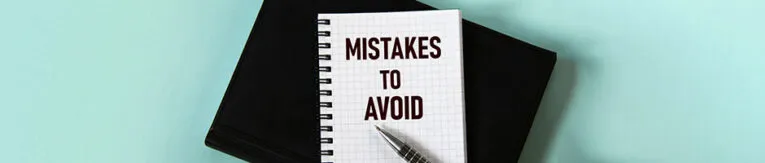 A notebook with the words "Mistakes to Avoid" written on the cover lies on top of a black folder, accompanied by a pen.