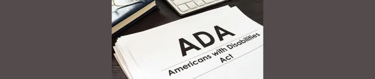 A book titled "ADA Americans with Disabilities Act" is displayed upright on a table with a gavel in front and a stack of books in the background.