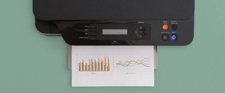 A black multifunction printer with a control panel is printing a document that displays several colorful bar and line graphs. The background is light green, providing an easy-to-understand guide on how to utilize and print lazy loaded images.