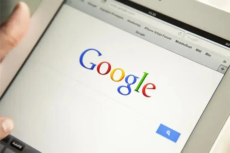 Person using a tablet with the Google search engine homepage displayed.