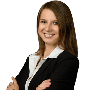 A woman with long brown hair, wearing a black blazer and white collared shirt, smiles with her arms crossed as PaperStreet celebrates International Women's Day with our clients.