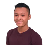 Man with short black hair wearing a maroon shirt smiles against a black background.