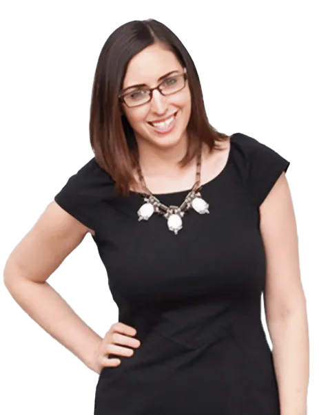 A woman with brown, shoulder-length hair and glasses is smiling. She is wearing a black dress and a necklace with white beads. She has one hand on her hip.