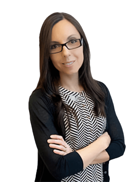 A woman with long dark hair and glasses stands with arms crossed, wearing a patterned dress and a black cardigan.