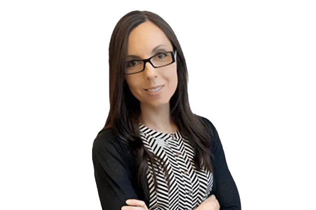 Woman with long dark hair and glasses in a black and white patterned top and black cardigan, standing with arms crossed.
