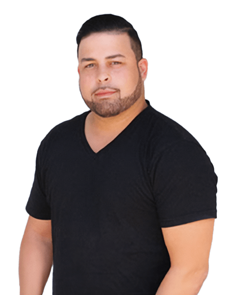 A man with short dark hair and a trimmed beard is wearing a black V-neck T-shirt. He is standing against a white background.