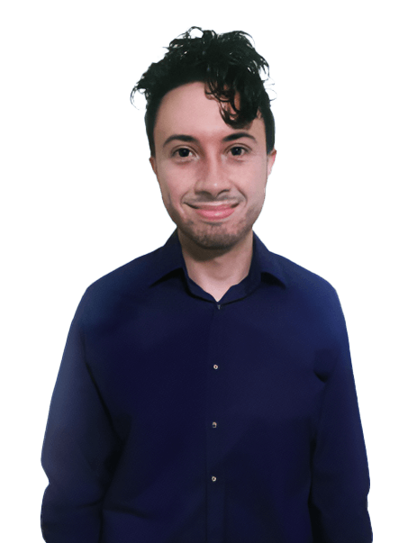 A person with curly dark hair, wearing a dark blue shirt, is standing and smiling at the camera against a plain white background.