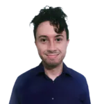 A person with dark curly hair wearing a blue shirt, smiling at the camera against a plain, dark background.