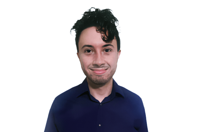 A person with dark curly hair wearing a blue shirt, smiling at the camera against a plain, dark background.