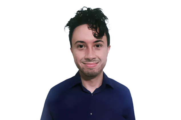 A person with dark curly hair wearing a blue shirt, smiling at the camera against a plain, dark background.