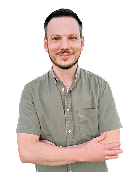 A man with short hair and a beard stands with his arms mildly crossed, wearing a short-sleeved, button-down shirt.