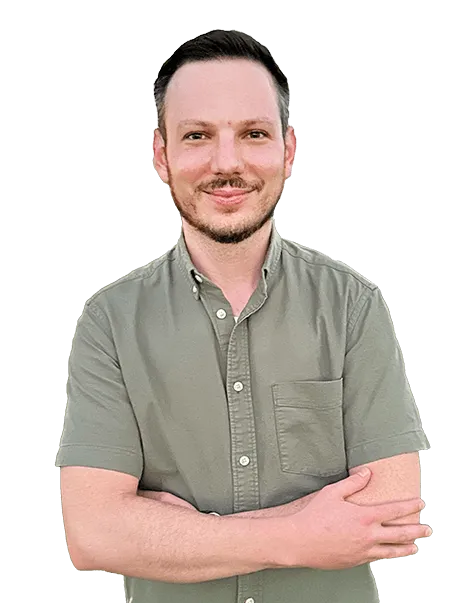 A man with short hair and a beard stands with his arms mildly crossed, wearing a short-sleeved, button-down shirt.