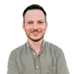 A man with short dark hair and a trimmed beard, wearing a button-up olive green shirt, stands against a plain white background.