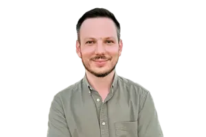 A man with short dark hair and a trimmed beard, wearing a button-up olive green shirt, stands against a plain white background.