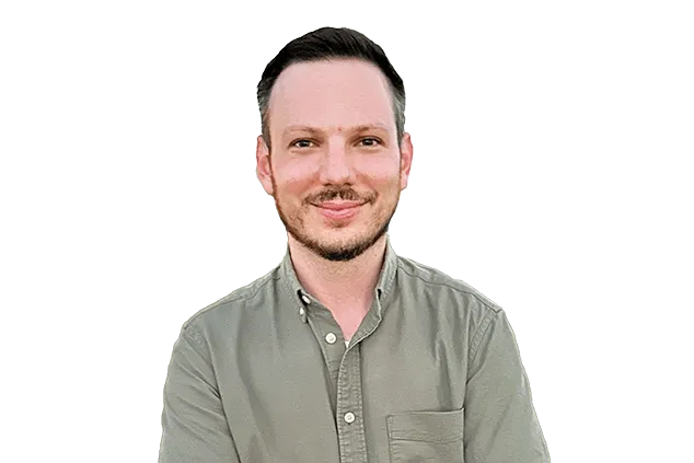 A man with short dark hair and a trimmed beard, wearing a button-up olive green shirt, stands against a plain white background.