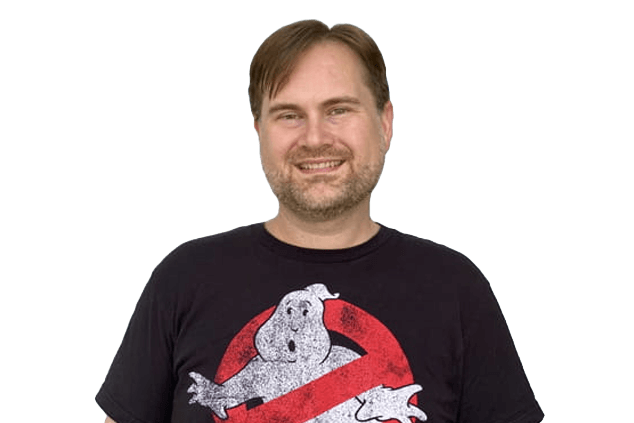 A man wearing a black "Ghostbusters" T-shirt smiles while standing against a white background.