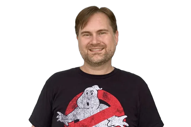 A man wearing a black "Ghostbusters" T-shirt smiles while standing against a white background.