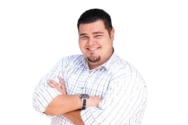 Smiling man with short hair and facial hair, wearing a white checkered shirt and a wristwatch, standing with arms crossed against a white background.