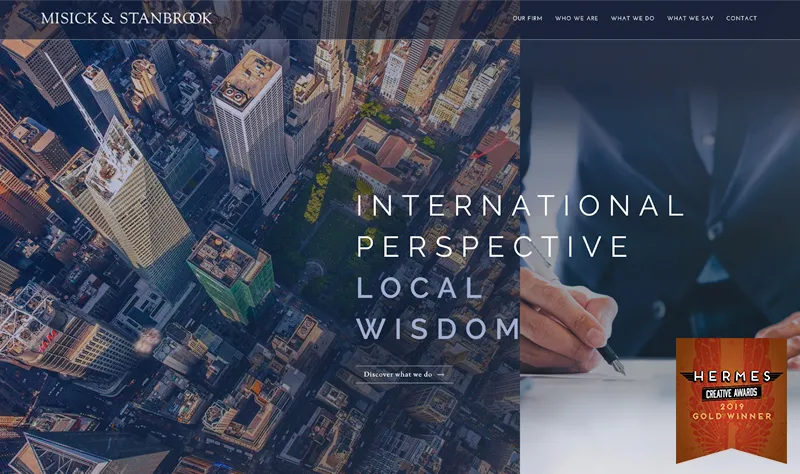 Aerial view of a city with a hand writing on paper overlay, text "Misick & Stanbrook, International Perspective, Local Wisdom." Hermes Creative Awards 2019 Gold Winner badge is at the bottom right.