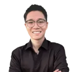 A person wearing glasses and a black shirt smiles with crossed arms in front of a plain, white background.