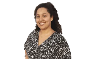 A person with curly hair, wearing a black and white patterned blouse, smiles at the camera.