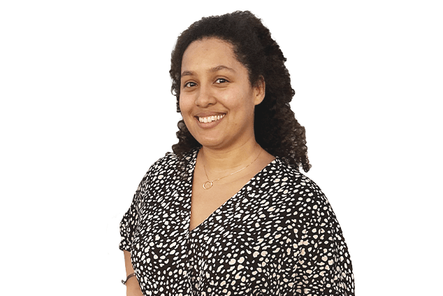 A person with curly hair, wearing a black and white patterned blouse, smiles at the camera.