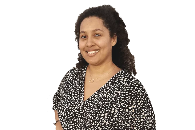 A person with curly hair, wearing a black and white patterned blouse, smiles at the camera.