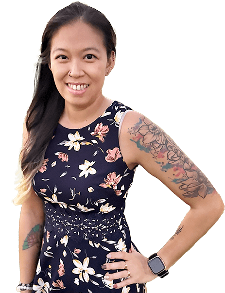 A woman in a floral dress smiles, displaying tattoos on her arms. She wears a smartwatch and has long, dark hair.