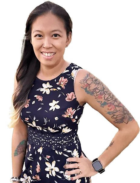 A woman in a floral dress smiles, displaying tattoos on her arms. She wears a smartwatch and has long, dark hair.
