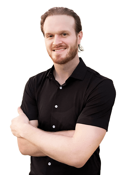 A man with a beard and shoulder-length hair, wearing a black short-sleeved shirt, stands with arms crossed, smiling.