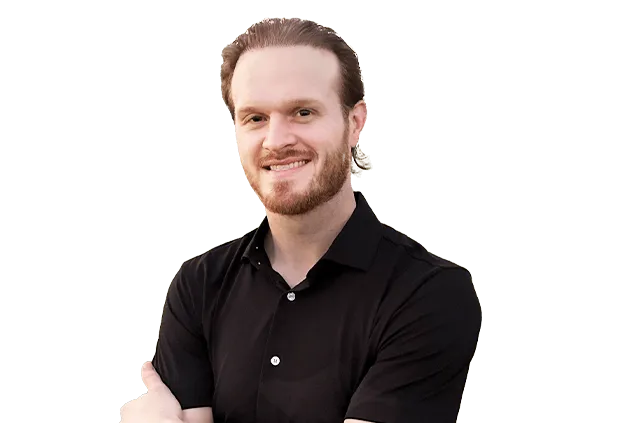 A man with light brown hair and a beard, wearing a black shirt, stands with arms crossed, smiling at the camera against a plain background.