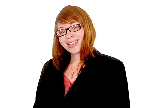 A smiling person with reddish-brown hair and glasses wearing a black blazer over a red shirt.