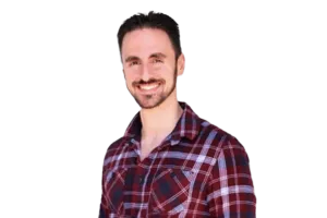 A man with dark hair and a beard smiles at the camera. He is wearing a red plaid shirt.