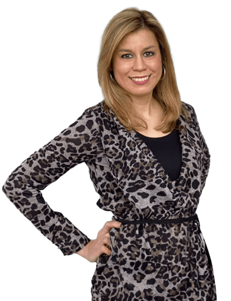 A woman stands with one hand on her hip, wearing a leopard print dress and smiling at the camera.