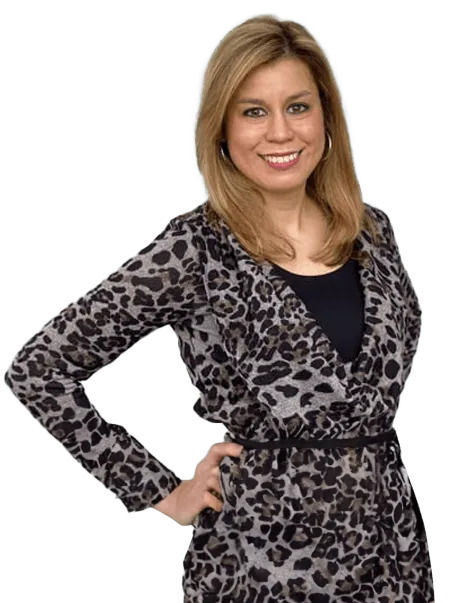 A woman stands with one hand on her hip, wearing a leopard print dress and smiling at the camera.