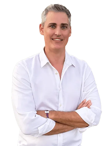 Man with short gray hair in a white shirt standing with arms crossed against a plain background.