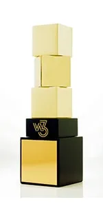 A golden and black W³ Award trophy featuring a design with stacked cubes on a black base.