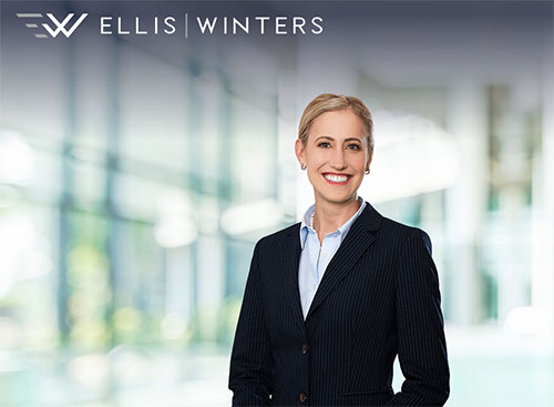 A smiling person in a dark pinstripe suit and light blue shirt stands in front of a blurred office background. The text "ELLIS | WINTERS" is at the top left corner.