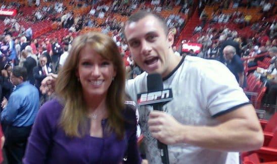 A woman and a man holding an ESPN microphone pose for a photo in a crowded indoor sports arena.