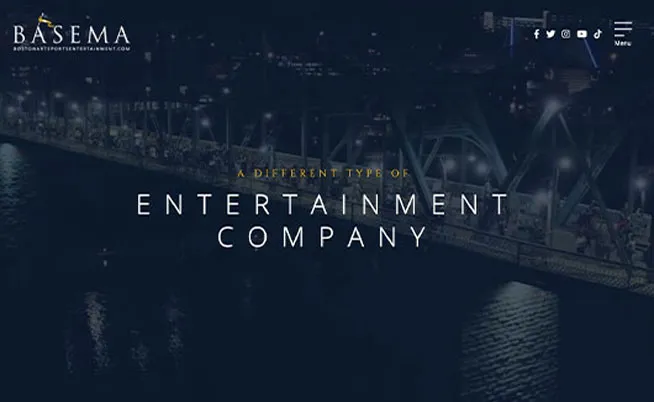 A night view of a city bridge filled with people, with text overlay saying "A Different Type of Entertainment Company" and the word "BASEMA" at the top left corner.